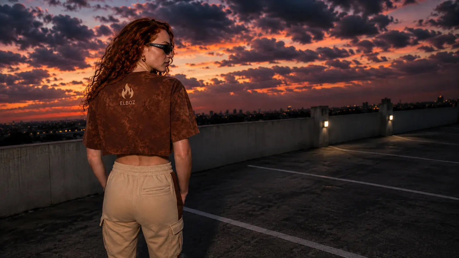 Modelo de costas no terraço ao pôr do sol, vestindo o cropped tie-dye marrom da Elboz